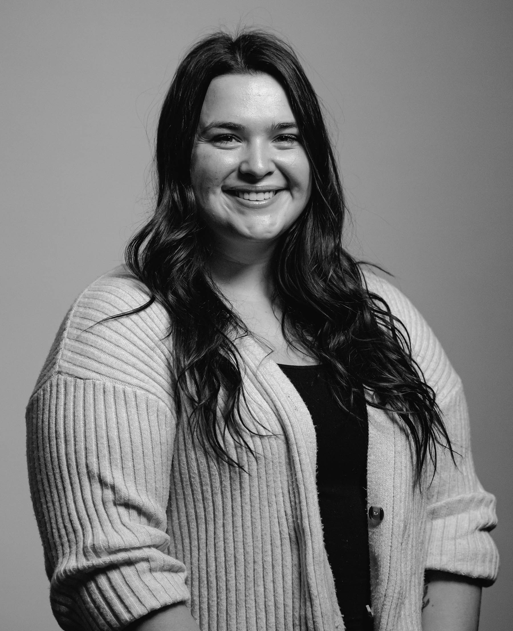 Kristen Milk, executive assistant, and community coordinator for Think 3D Solutions, long curled, dark hair, bright smile, light cardigan with rolled sleeves, lighter complexion, black shirt underneath, the photo is in black and white.