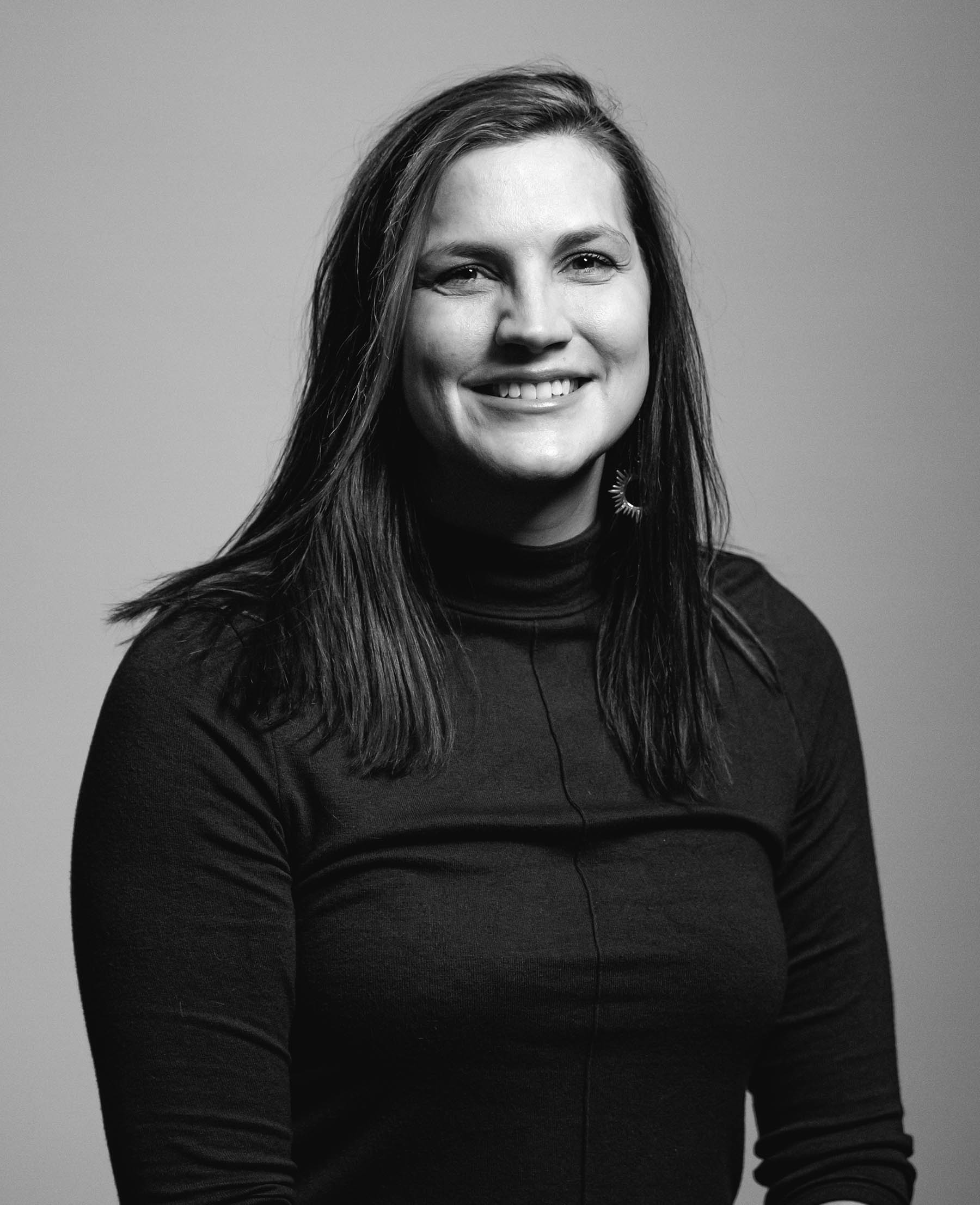 Megan Jung, brand and marketing director for Think 3D Solutions, smiling, with darker hair just past shoulder, dark turtleneck sweater, light skin completion, the photo is in black and white.