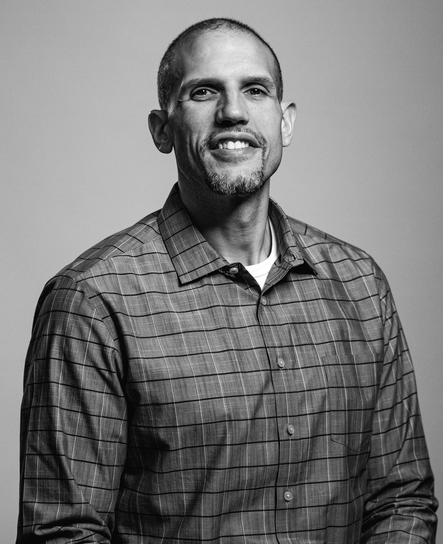 Tamien Dysart, CEO and co-founder of Think 3D Solutions, is sitting and smiling in a plaid button-up shirt, he has a goatee, and short dark hair, the photo is in black and white.